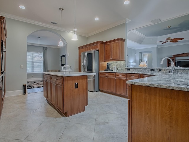 kitchen featuring stainless steel refrigerator with ice dispenser, kitchen peninsula, ornamental molding, decorative light fixtures, and ceiling fan with notable chandelier