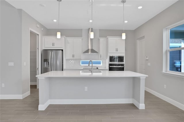 kitchen featuring appliances with stainless steel finishes, decorative light fixtures, white cabinetry, and wall chimney range hood