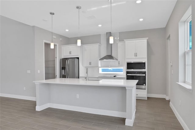 kitchen with pendant lighting, a kitchen island with sink, white cabinets, wall chimney range hood, and stainless steel appliances