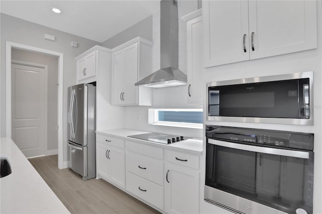 kitchen featuring tasteful backsplash, white cabinetry, stainless steel appliances, and wall chimney range hood