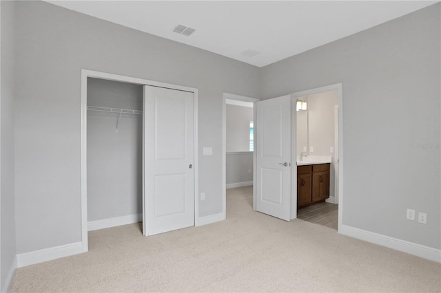 unfurnished bedroom with ensuite bath, light colored carpet, and a closet