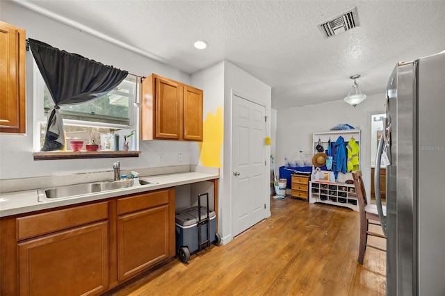 kitchen with sink, light wood-type flooring, a textured ceiling, stainless steel fridge, and decorative light fixtures