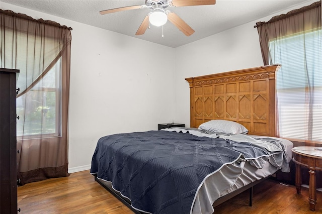 bedroom with a textured ceiling, wood-type flooring, and ceiling fan