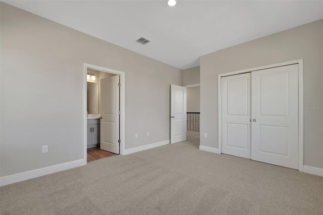 unfurnished bedroom with light carpet, ensuite bath, and a closet