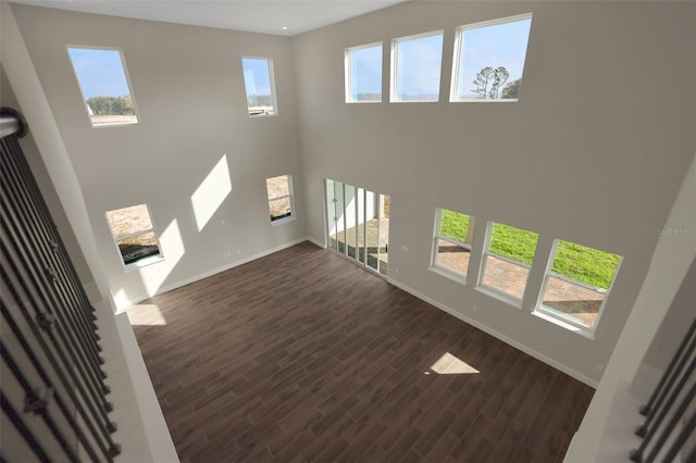 unfurnished living room with a high ceiling, dark wood-type flooring, and a wealth of natural light