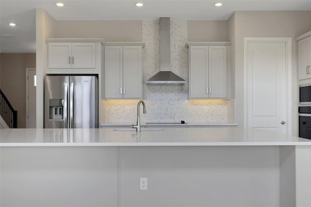 kitchen featuring sink, a large island with sink, wall chimney range hood, stainless steel fridge, and white cabinets