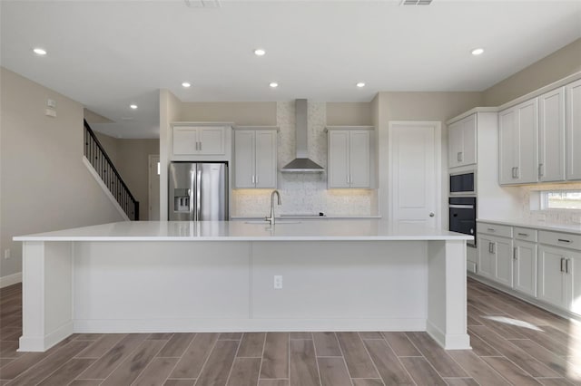 kitchen featuring black oven, built in microwave, stainless steel fridge with ice dispenser, a spacious island, and wall chimney exhaust hood