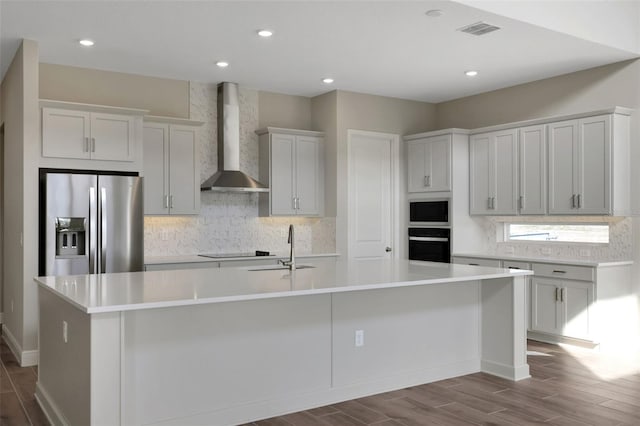 kitchen featuring hardwood / wood-style floors, sink, a large island with sink, black appliances, and wall chimney exhaust hood