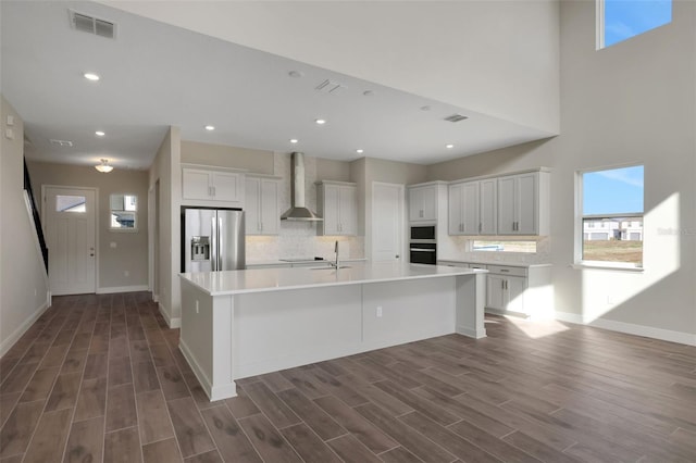 kitchen featuring white cabinetry, wall chimney range hood, a spacious island, black oven, and stainless steel fridge with ice dispenser