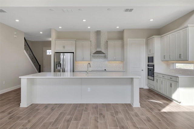 kitchen featuring appliances with stainless steel finishes, white cabinets, wall chimney range hood, and a large island