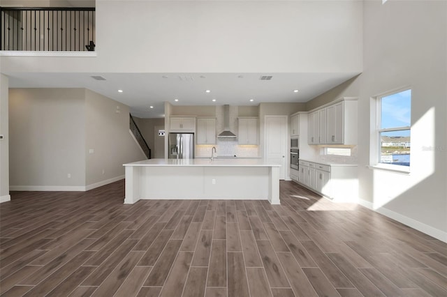 kitchen featuring appliances with stainless steel finishes, white cabinetry, dark hardwood / wood-style flooring, wall chimney exhaust hood, and a kitchen island with sink