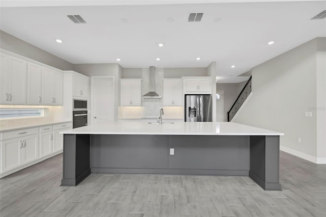 kitchen featuring white cabinets, wall chimney exhaust hood, stainless steel fridge, and a large island