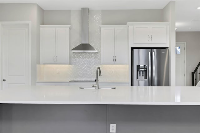 kitchen with sink, stainless steel refrigerator with ice dispenser, white cabinetry, wall chimney exhaust hood, and decorative backsplash