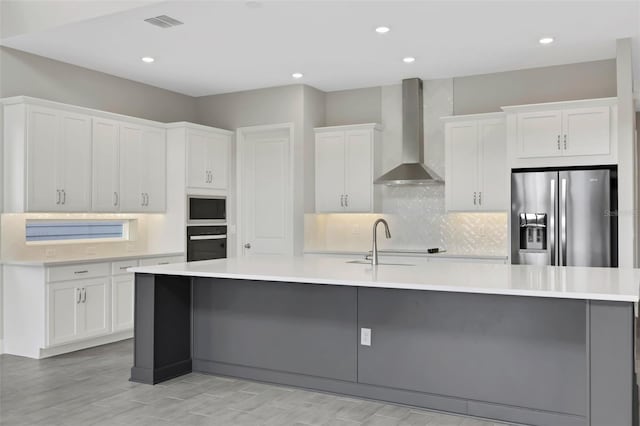 kitchen featuring white cabinets, a large island, wall chimney range hood, and stainless steel refrigerator with ice dispenser