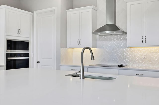 kitchen with wall chimney exhaust hood, oven, white cabinets, stainless steel microwave, and decorative backsplash