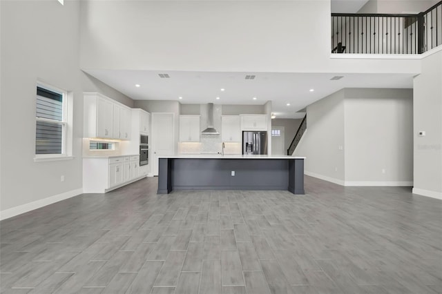 kitchen featuring stainless steel fridge with ice dispenser, a spacious island, a breakfast bar, white cabinets, and wall chimney range hood