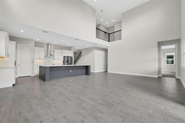 kitchen featuring wall chimney exhaust hood, white cabinetry, a large island with sink, and stainless steel refrigerator with ice dispenser