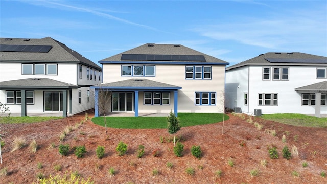 back of property with central AC, solar panels, a patio area, and a lawn