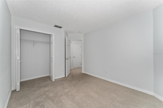 unfurnished bedroom with light carpet, a textured ceiling, and a closet