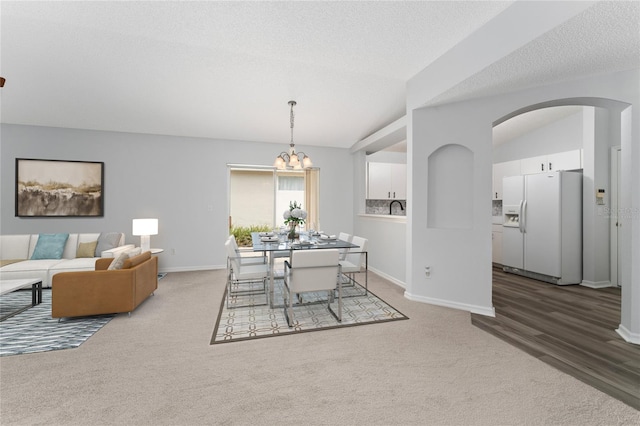 carpeted dining room with an inviting chandelier, a textured ceiling, and vaulted ceiling