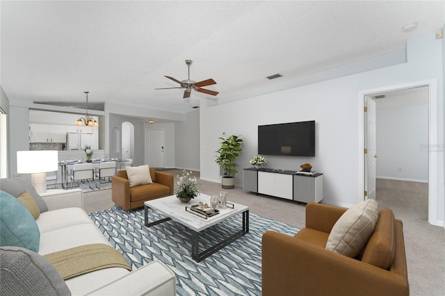 carpeted living room featuring a textured ceiling and ceiling fan with notable chandelier