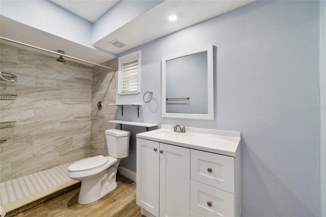 bathroom featuring a tile shower, vanity, toilet, and hardwood / wood-style floors