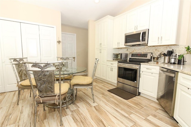 kitchen featuring white cabinets, decorative backsplash, appliances with stainless steel finishes, light hardwood / wood-style floors, and light stone counters