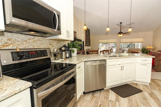 kitchen featuring light stone countertops, appliances with stainless steel finishes, kitchen peninsula, sink, and white cabinetry