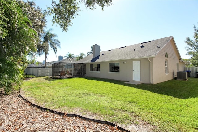 rear view of house featuring central AC unit, glass enclosure, and a lawn