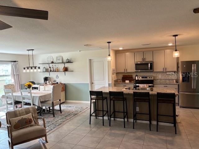 kitchen with sink, stainless steel appliances, a kitchen breakfast bar, decorative light fixtures, and light tile patterned flooring