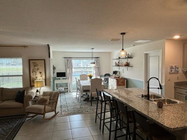 kitchen with a breakfast bar, a textured ceiling, sink, pendant lighting, and light tile patterned floors