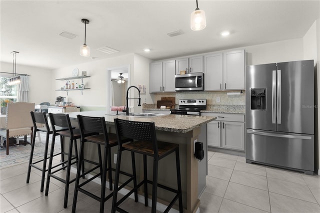 kitchen with pendant lighting, stainless steel appliances, a kitchen island with sink, and gray cabinetry