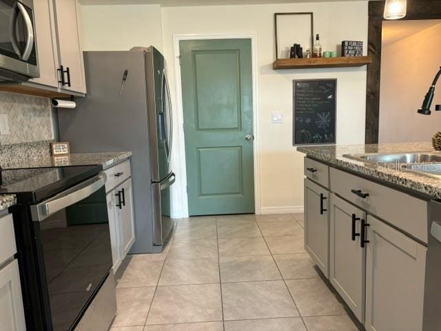 kitchen featuring light tile patterned flooring, appliances with stainless steel finishes, gray cabinetry, and dark stone countertops