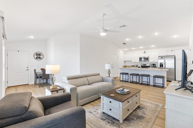 living room with ceiling fan, vaulted ceiling, and light wood-type flooring