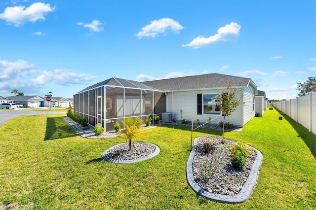 view of front of house with central AC, glass enclosure, and a front lawn