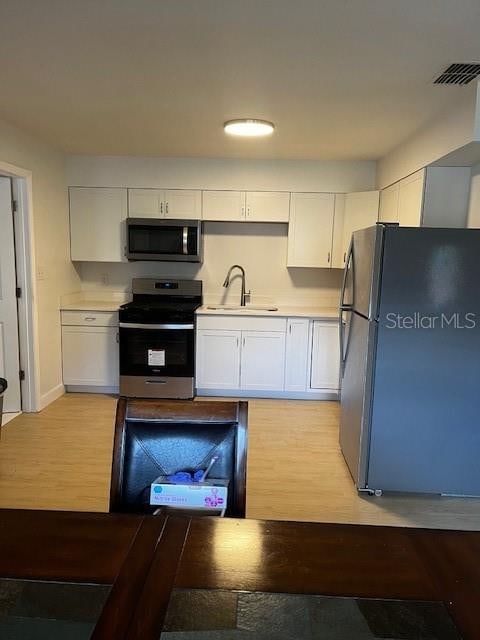 kitchen with sink, appliances with stainless steel finishes, light hardwood / wood-style flooring, and white cabinetry