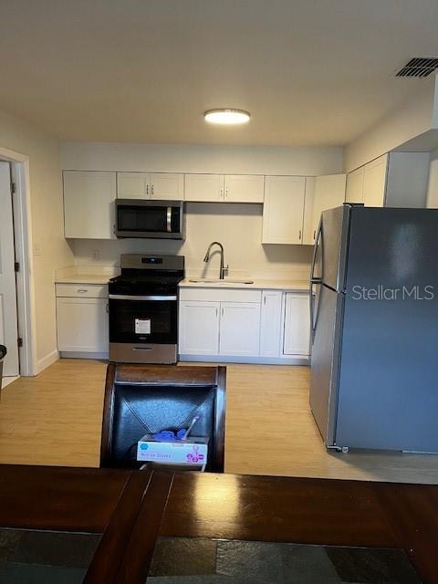 620 Gould St, Eustis, FL 32726 - kitchen featuring appliances with stainless steel finishes, a sink, white cabinetry, light countertops, and light wood-type flooring
