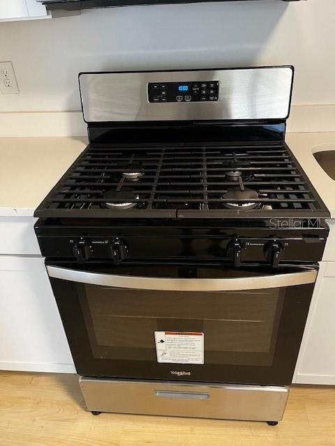 interior details with stainless steel gas stove, white cabinetry, and light hardwood / wood-style flooring