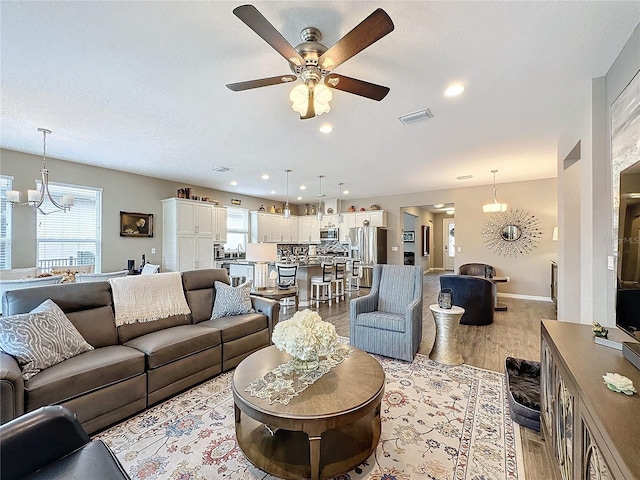 living room with ceiling fan with notable chandelier, light wood-type flooring, and a healthy amount of sunlight