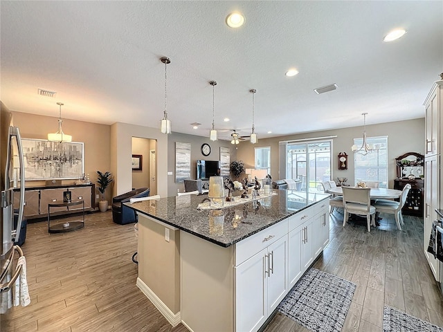 kitchen with dark stone countertops, a center island, decorative light fixtures, light wood-type flooring, and white cabinetry