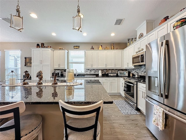 kitchen with hanging light fixtures, a kitchen island, dark stone counters, appliances with stainless steel finishes, and a kitchen breakfast bar