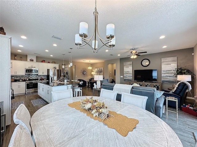 dining space featuring ceiling fan with notable chandelier, dark wood-type flooring, and a textured ceiling