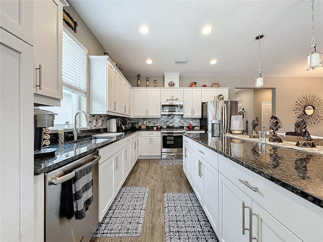 kitchen featuring appliances with stainless steel finishes, white cabinetry, hardwood / wood-style flooring, and hanging light fixtures