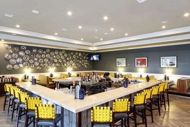 bar with parquet floors, a tray ceiling, and light stone countertops