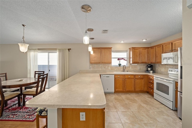 kitchen with a wealth of natural light, sink, pendant lighting, and white appliances