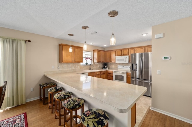 kitchen with kitchen peninsula, a kitchen bar, light hardwood / wood-style flooring, pendant lighting, and white appliances