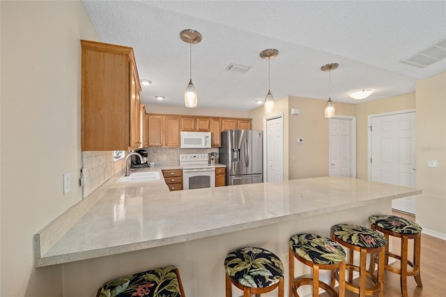 kitchen featuring a kitchen breakfast bar, kitchen peninsula, white appliances, sink, and light hardwood / wood-style floors