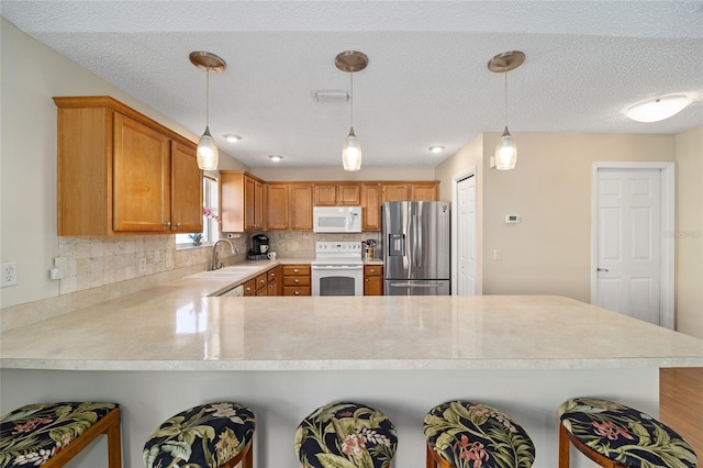 kitchen featuring kitchen peninsula, hanging light fixtures, a breakfast bar area, backsplash, and white appliances