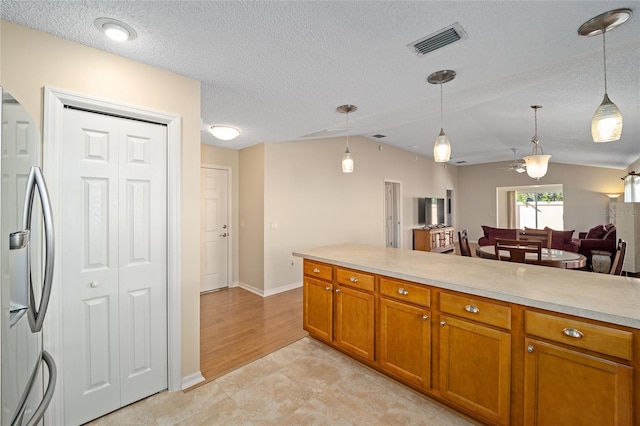 kitchen featuring light wood-type flooring, a textured ceiling, pendant lighting, and stainless steel fridge