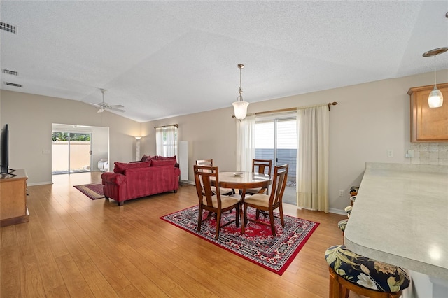 dining space with light hardwood / wood-style flooring, a textured ceiling, vaulted ceiling, and ceiling fan